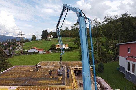 Arbeiter befinden sich gerade am Hausdach - mit der Betonpumpe wird gerade die Decke betoniert.